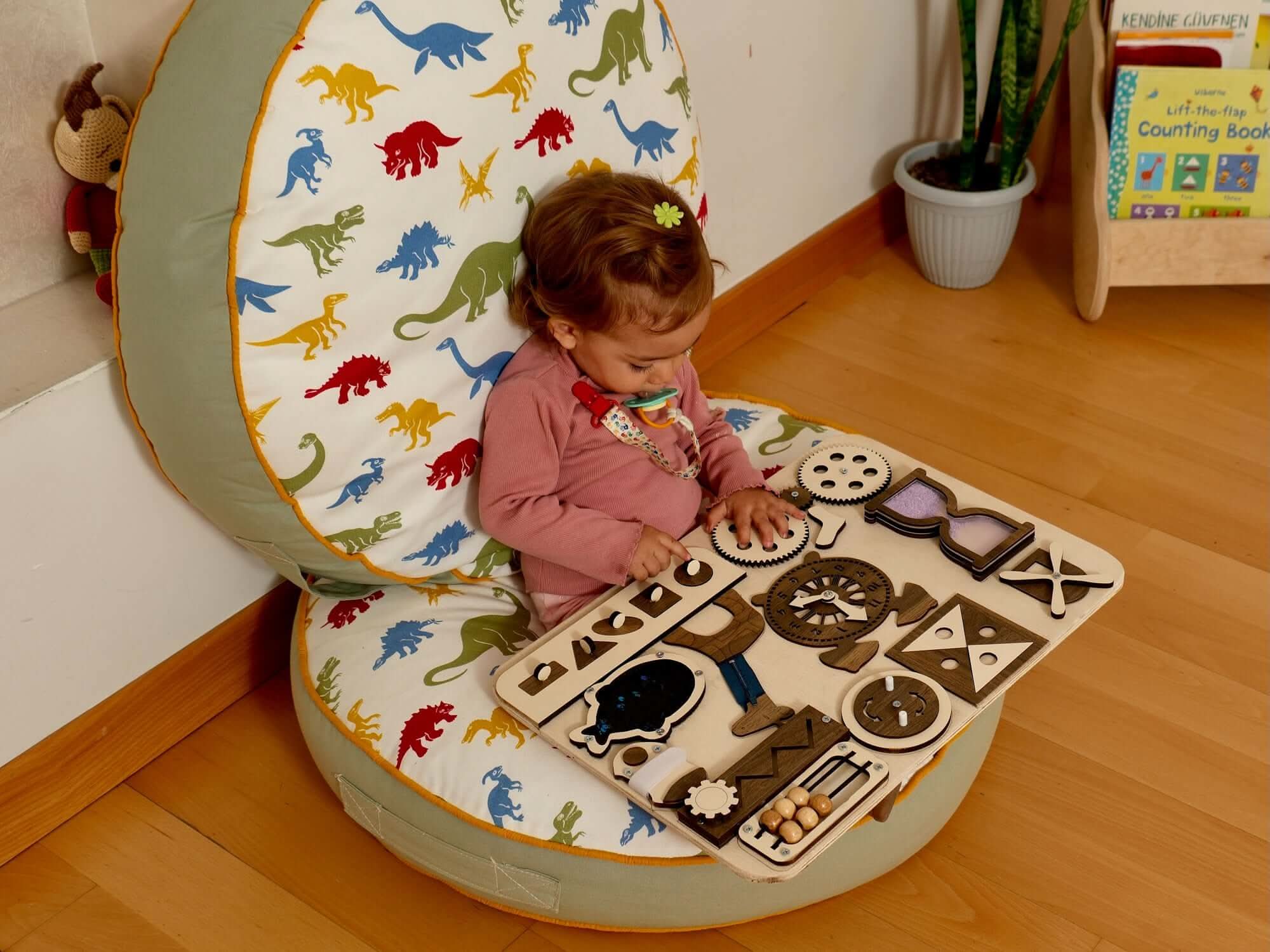Toddler engaged in hands-on learning with a wooden activity board on a dinosaur-patterned seat.