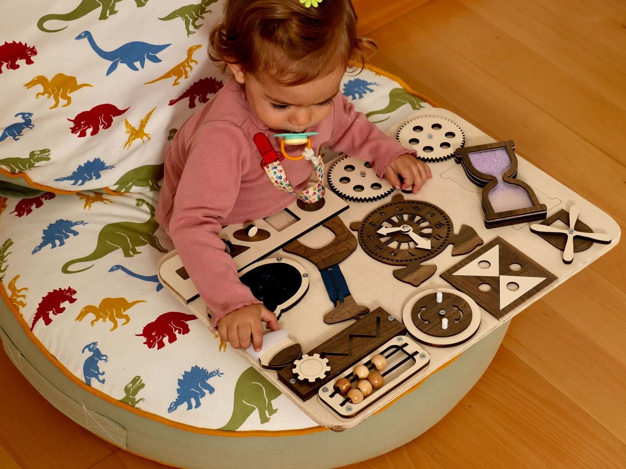 Toddler engaged with a Wooden Busy Board, exploring gears and shapes on a colorful cushioned seat.