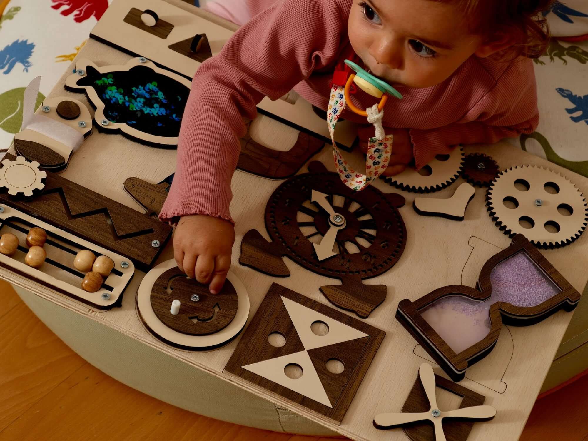 Toddler exploring a Montessori-inspired wooden busy board with various interactive activities, supporting sensory play.