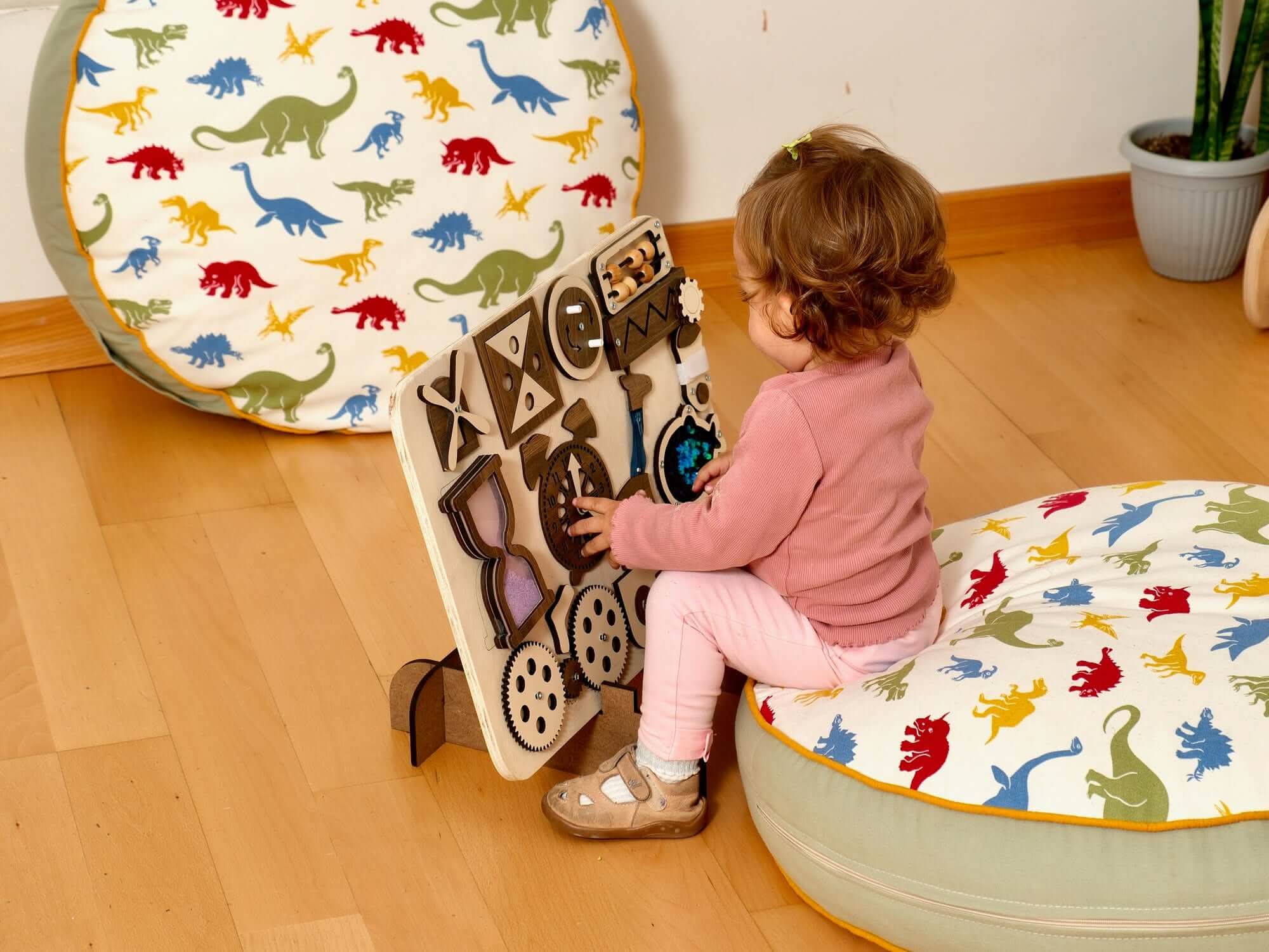 Toddler exploring a Montessori-inspired Wooden Busy Board activity toy on a colorful floor cushion.