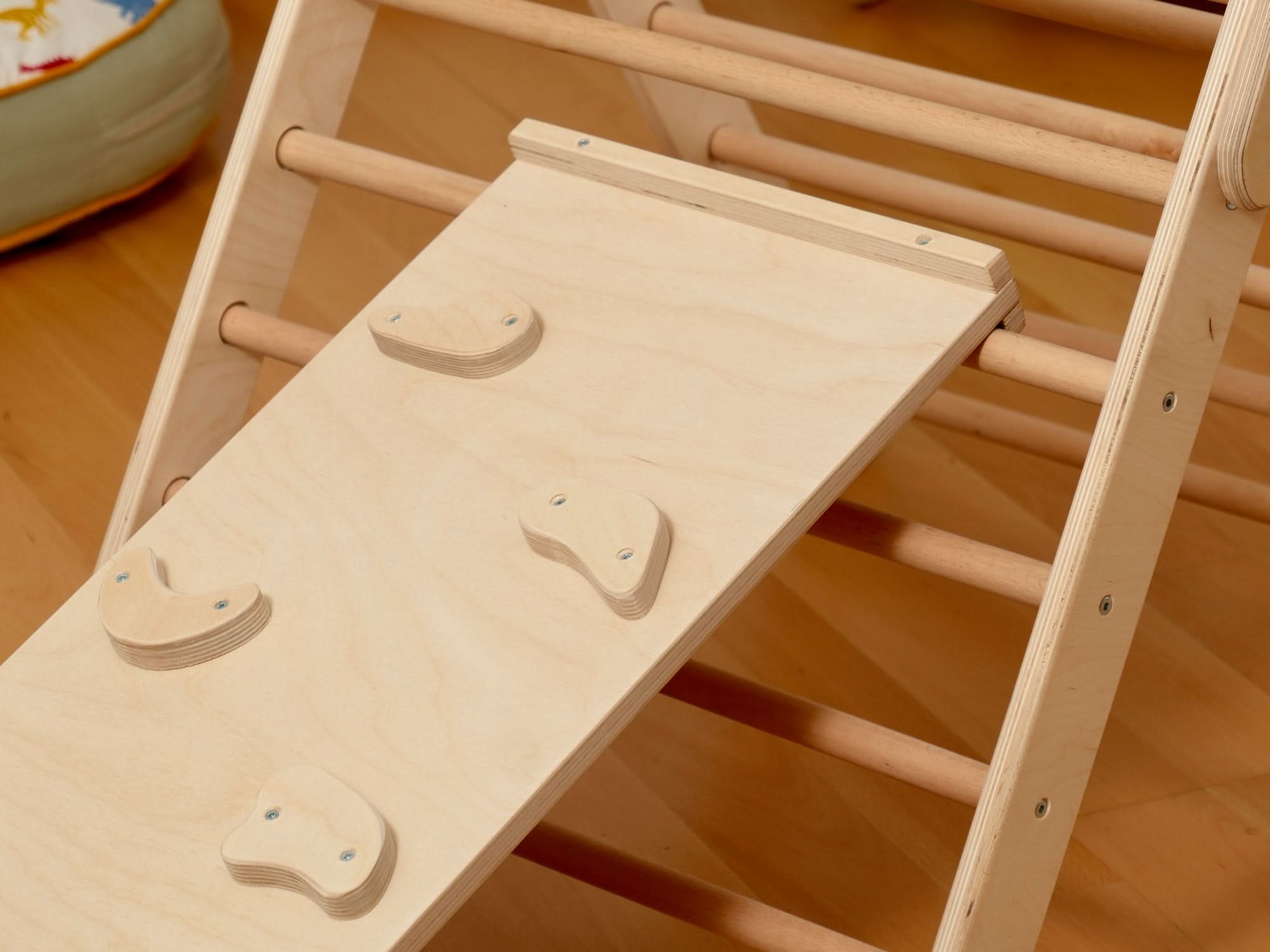 Close-up of Pikler triangle climbing ramp with grip holds for toddlers in a Montessori indoor playground.
