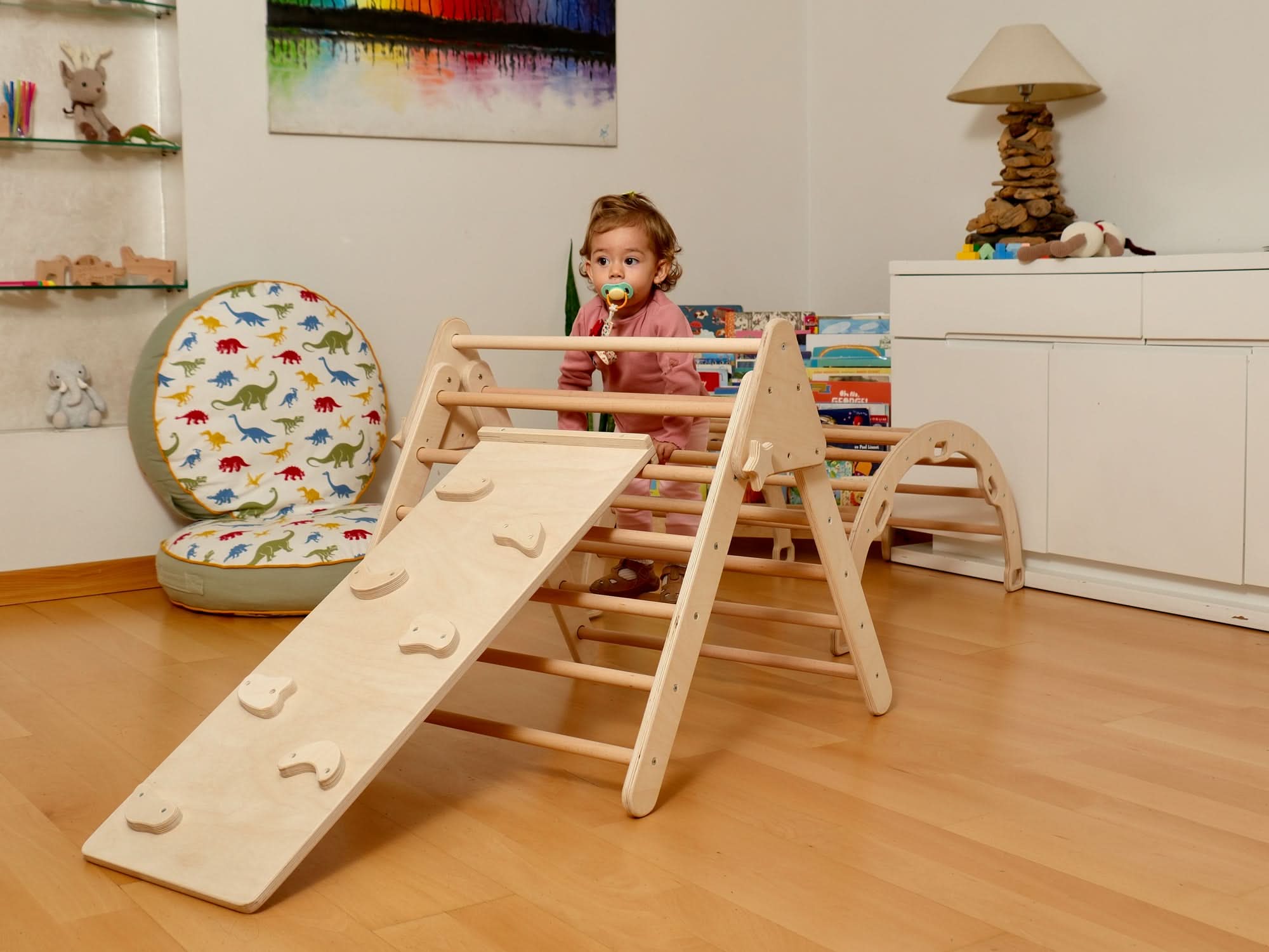 Toddler enjoying a Montessori indoor playground with a Pikler triangle and climbing arch on a wooden floor.