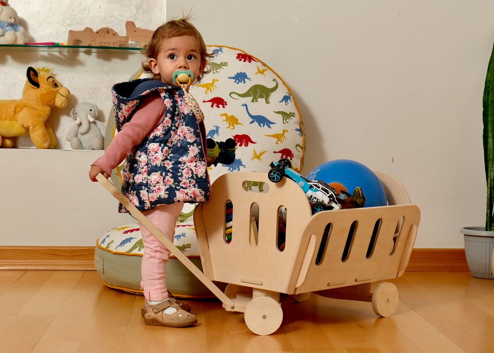 Toddler pulling a Montessori wooden toy cart, surrounded by playful decor in a cozy playroom.
