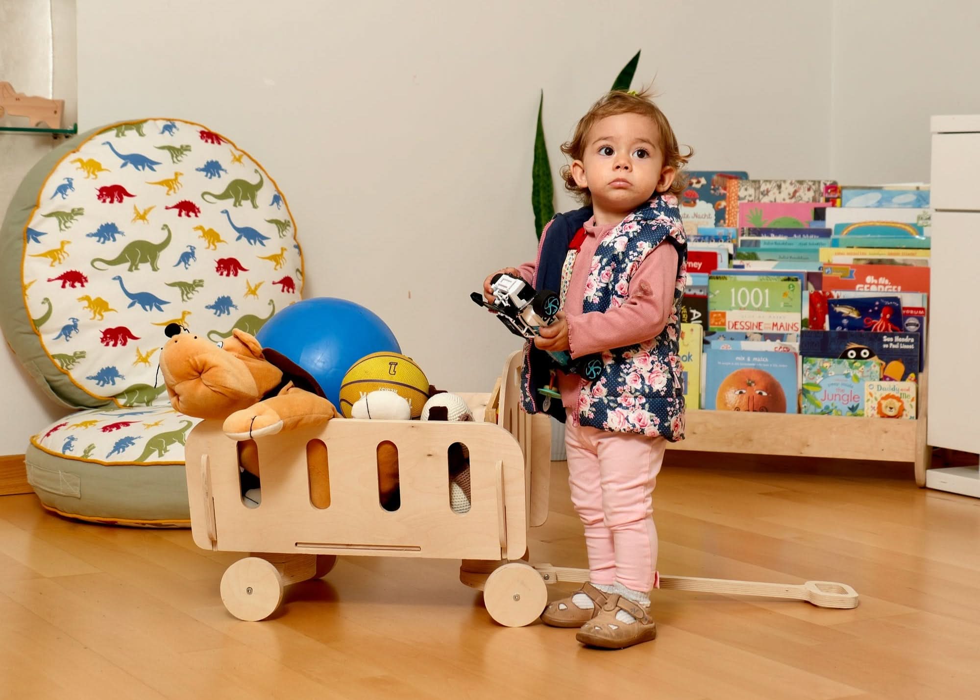 Toddler enjoying a Montessori wooden toy storage cart filled with plush toys and balls in a bright playroom.